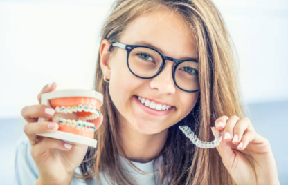 A girl with glasses holds a toothbrush and braces, showcasing the expertise of cosmetic dentists.