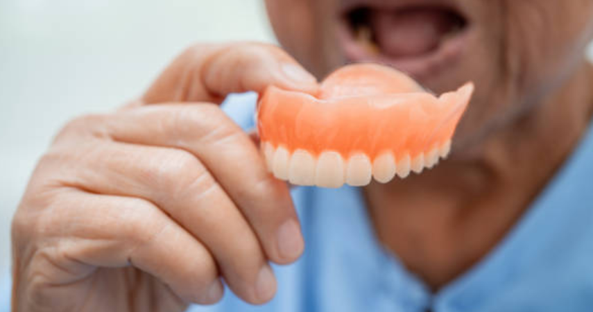 A person holding a denture that helps as a convenient and flexible solution for missing teeth.