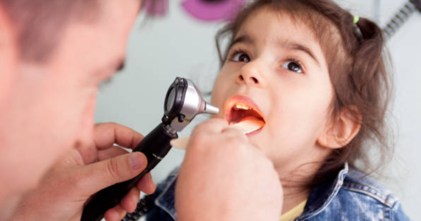 A child sitting in a dentist's chair, getting examined by a dentist with tools and torch in hand