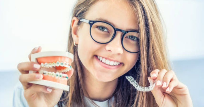 A girl with glasses holds a toothbrush and braces, showcasing the expertise of cosmetic dentists.